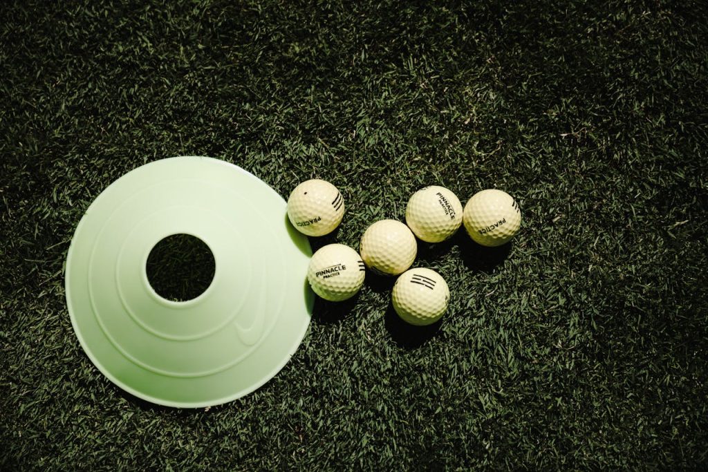White golf balls and a training cone placed on vibrant green grass, ready for practice.