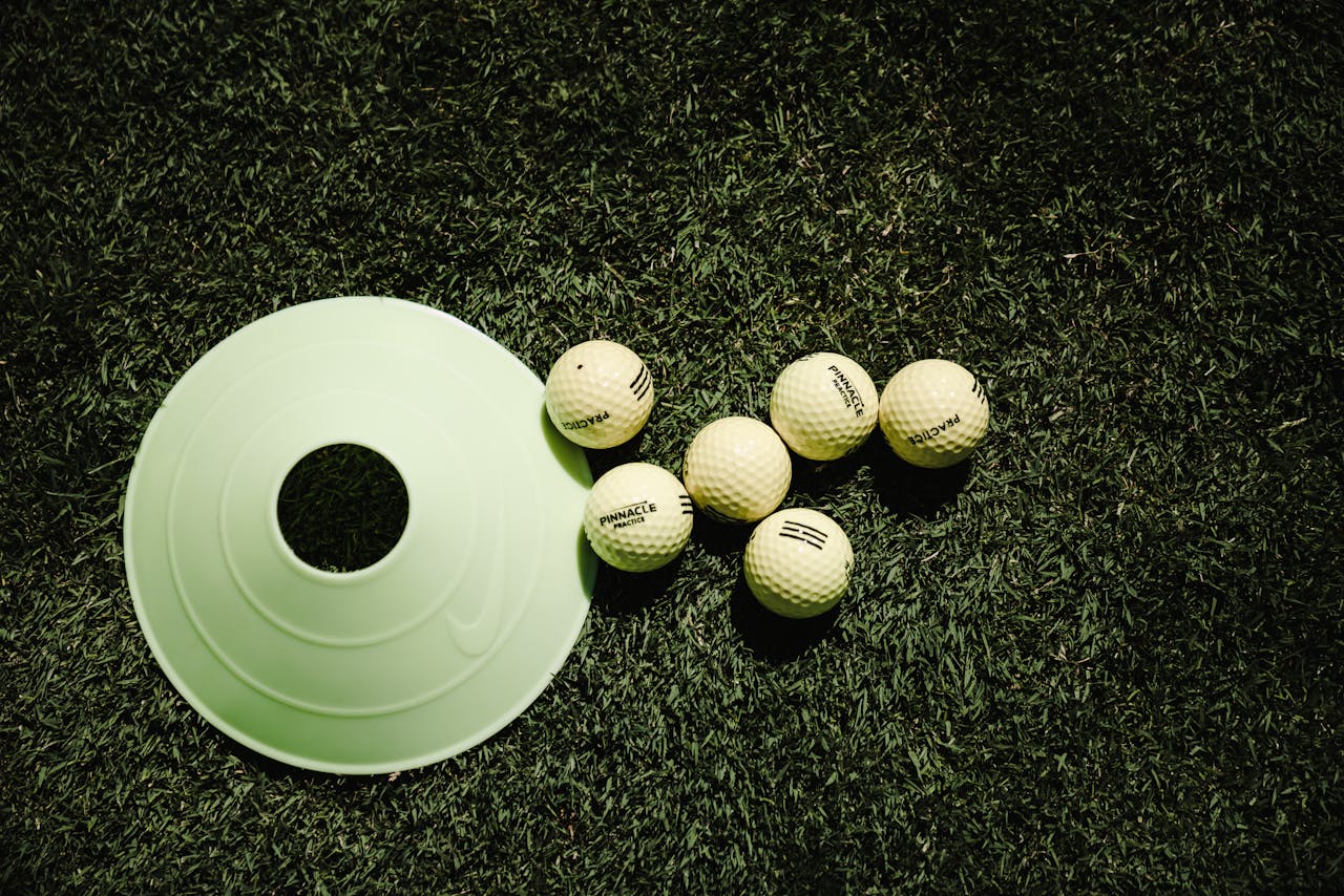 White golf balls and a training cone placed on vibrant green grass, ready for practice.